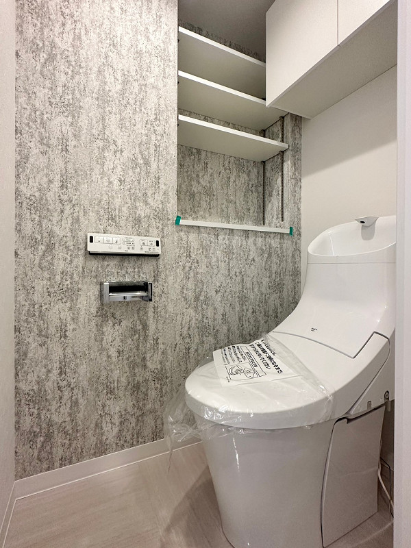 トイレ　ノア新宿1号館 トイレスペースは、グレーを基調としたクロスが落ち着いた印象を与えてくれていますよ。嬉しい温水洗浄便座付きです。収納スペースもしっかりとあるので、トイレットペーパーやお掃除道具の収納には困りません。