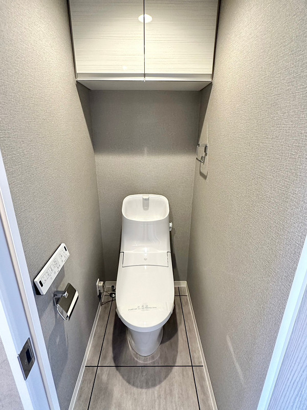 トイレ 温水洗浄便座付きのトイレは廊下の独立スペースにありました。グレーのクロスが施されたシンプルな空間です。なんと手洗い一体型は節水効果があるんですよ。トイレットペーパーなどの備品は吊戸棚にしまいましょう。