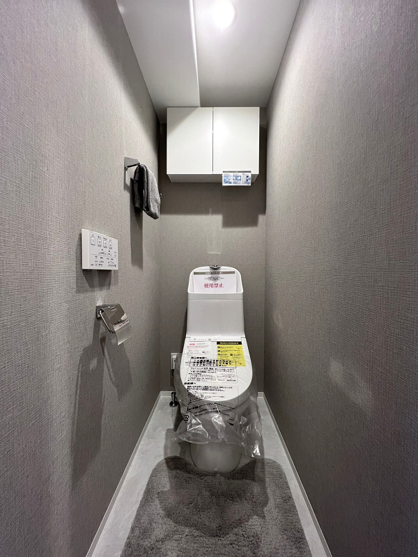 トイレ　レックス西早稲田 グレートーンでまとめられた落ち着きのあるトイレは、サニタリールームとは別の独立空間。節水効果が見込まれる手洗い一体型を採用しています。便器には特殊加工が施され、汚れが落ちやすくお手入れが楽に行えるんですよ。トイレットペーパーなどの備品は吊り戸棚へどうぞ。