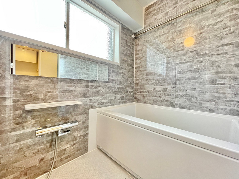 第二梅ヶ丘ハイム　バスルーム バスルームはグレーの石タイル風パネルを使用し、高級感のあるデザインとなりました。何かと便利な鏡付き♪浴室乾燥機を備えている上に窓があり、湿気対策はバッチリです。さらに追い焚き機能も搭載しているので、入浴時に寒い思いをすることはなさそうですね。