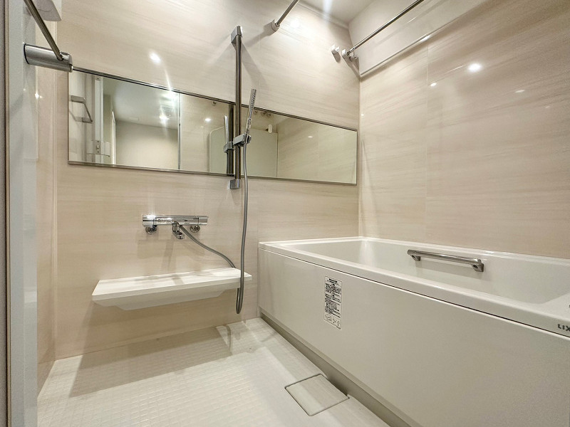 コーポ小石川　バスルーム ベージュのパネルが施されたバスルーム。ワイドなミラーは空間を広く見せてくれる効果があるんですよ。天候を気にせずお洗濯ができる浴室乾燥機付き。バスタブには追い焚き機能が搭載されているので、いつでも温かいお風呂に入ることができます。