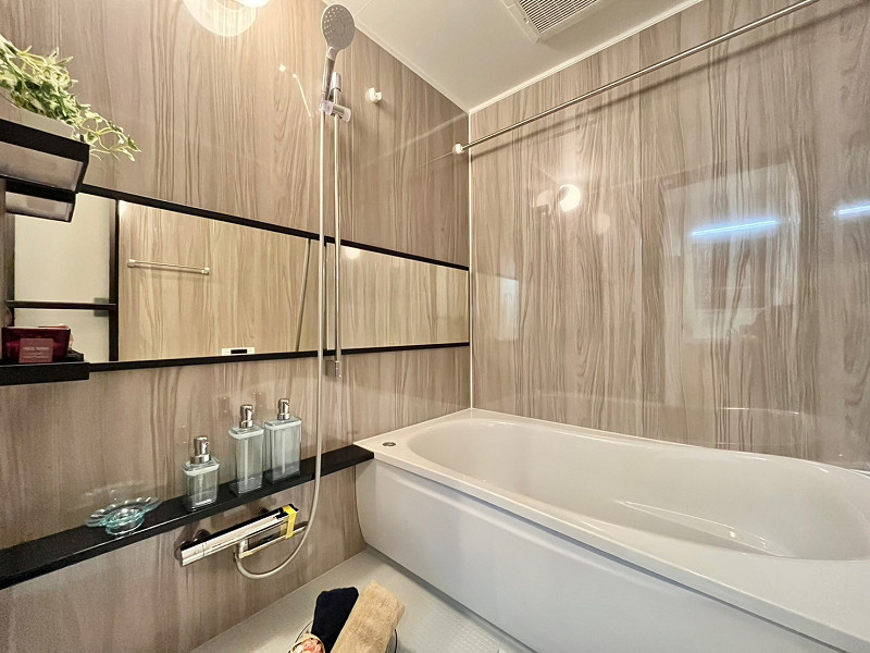 日生野沢マンション　浴室 ワイドな鏡が空間に奥行きを与えてくれるバスルーム。ゆったりとした1416サイズです。柔らかな色合いの木目調パネルに黒が程よいアクセントになっていますね。浴室乾燥機＆追い焚き機能を搭載し、いつでも快適なバスタイムを過ごせます✦
