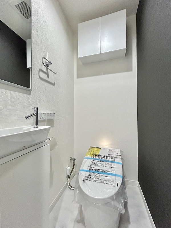 ライオンズマンション日本橋　トイレ グレーのアクセントクロスが用いられ、スタイリッシュな雰囲気のトイレ。すっきりとした見た目のタンクレスタイプのトイレは、凹凸が少ない分お手入れがしやすいというメリットがあるんですよ。温水洗浄便座機能と独立した手洗い場があるので、お客様にも快適にご利用いただけますね⭐