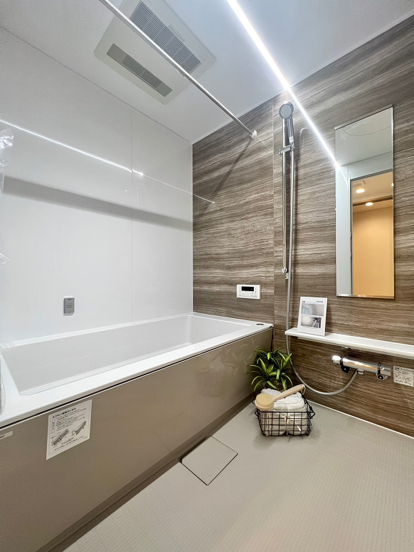 千石三丁目シティハウス　バスルーム 木目の鏡面パネルがアクセントのバスルームはフラットラインLED照明をセレクトし、ラグジュアリーな雰囲気に。照明は調色ができるので、灯りの色を切り替えてバスタイムを豊かに演出してくれますよ。追い焚き機能や浴室乾燥機を活用し極上のバスタイムをご堪能くださいね。