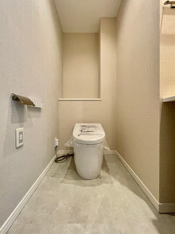 カテリーナ三田タワースイート　トイレA 大理石風のフロアタイルが清潔感あふれるトイレはタンクレスタイプですっきりとした印象に。目の前に立つと自動でふたが開くセンサー付きなので触れることなく衛生的に保てます。写真右手側にはコンパクトな手洗い器を設置し、移動することなく手洗いまで済ませられるスムーズな動線を確保♪ 