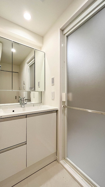 エンゼルハイム大森第8　洗面室 パウダールームはコンパクトにまとめ、その分居室やキッチンを広く確保しました。掃除機やモップ掛けがしやすいのも嬉しいポイントです。正面に設置された洗面化粧台は3面鏡型で、ヘアセットやメイクに便利◎