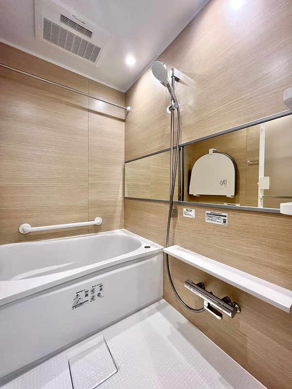 マートルコート豪徳寺　バスルーム 今回のリノベーションで新規交換されたバスルームは艶消しタイプの木目パネルをセレクトし、柔らかくナチュラルな印象。ワイドミラーを取り入れたことで空間に奥行きが生まれ広く感じられました。追い焚き機能や浴室乾燥機を活用し、快適なバスタイムをご堪能くださいね。
