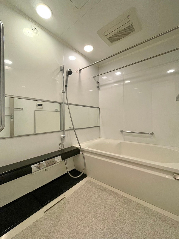 アトラスタワー西新宿　バスルーム バスルームは白×ブラックのモノトーン調に仕上がり、清潔感たっぷり。ワイドな鏡が空間に奥行きをプラスし、広やかに感じられます。ライトはダウンライトを採用し、よりオシャレに。浴室乾燥機を使って、カビ知らずの清潔な空間を保ちましょうね。バスタブには手すりやアームレスト、腰掛段差がついています。追い焚き機能を活用すれば、快適な半身浴ができそうです。