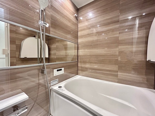 コーヅ第5大森　バスルーム ブラウンの艶やかなパネルが高級感を醸し出しているバスルーム🛀ワイドな鏡が開放感をもたらしていますね。丸みを帯びたバスタブは体にフィットし、1日の疲れをしっかり癒してくれるはず。オートバス機能や追い焚き機能を搭載しているため、いつでも温かいお風呂に入ることができるのも魅力的。さらに、部屋干しに便利な浴室換気乾燥機も完備。
