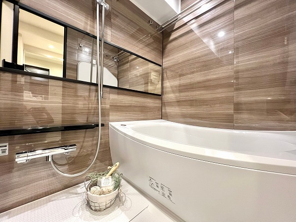 江戸川橋センチュリープラザ21　バスルーム横向き 高級感漂う木目のパネルを採用したバスルームは、ブラックがアクセントとなりスタイリッシュな印象。ワイドミラーをセレクトしたことで、空間がさらに広々と感じられました。追い焚き機能や浴室乾燥機を活用して毎日快適なバスタイムをご堪能くださいね。