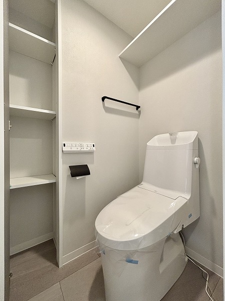 月島ホームズ_シンプルなトイレの写真 玄関右手には、清潔感たっぷりの白基調の独立トイレが。節水タイプの手洗い一体型トイレと温水洗浄便座を備えており、冬でも快適にご使用いただけます。吊戸棚や可動棚の収納も充実しているため、掃除用品や日用品もすっきり片付きますね！