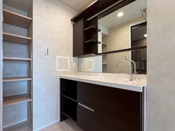ライオンズマンション西蒲田_洗面化粧台の写真 パウダールームも玄関と同様にシックな配色で一見シンプルなデザインですが、収納の配置、開き方が個性的な印象でした。鏡と同じ高さに設置された収納は、開閉式の収納とオープン収納の組み合わせとなっており、使用頻度ごとに収納を分けられる造りになっています。