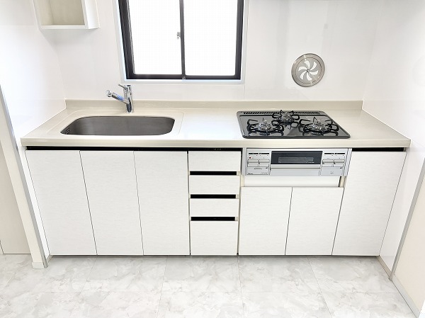 ライオンズマンション松原第2_リノベーション済みのキッチンの写真 システムキッチンは作業に集中しやすい壁付け型なので、日々の家事効率のアップが望めます♪目の前に窓があるため、すぐに換気をすることができ匂いがこもってしまう心配はありません。複数品同時に調理可能な3口コンロとグリル付きで料理が捗りそう。